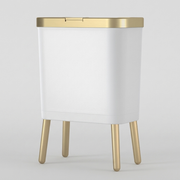 A modern white rectangular side table or stool with a brushed gold metal top trim and four tapered gold legs, shown on a light gray studio background.