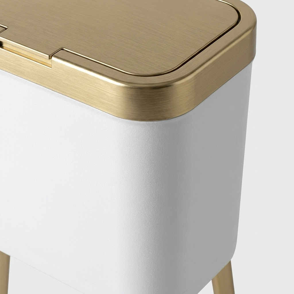 Close-up of a modern rectangular trash can with a brushed gold metal lid and legs, and a white body, shown on a light gray background.