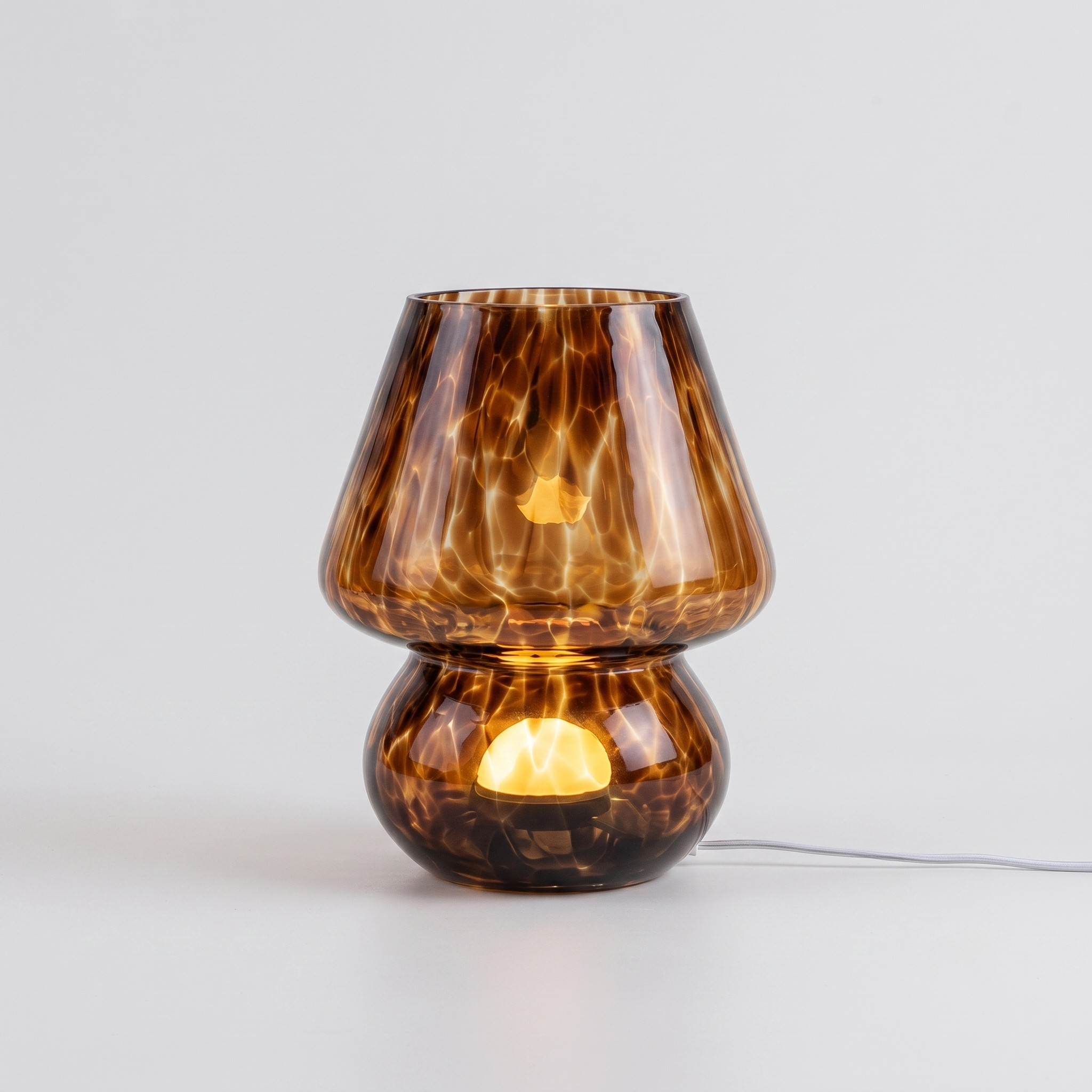 A modern amber glass table lamp with a flared top and rounded base, illuminated from within against a clean light gray background.
