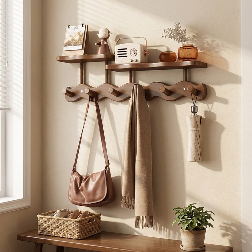 A wall-mounted wooden entryway shelf and coat rack set styled in a warm, sunlit room. The dark brown wood rack features two upper shelves holding decorative items, a wavy middle section with five hanging hooks holding a brown shoulder bag, a beige scarf, and a cream umbrella, and a lower shelf holding a woven basket and a small potted plant.