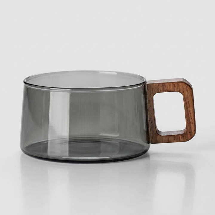 A translucent smoky gray glass mug with a square wooden handle, shown on a clean white reflective surface.