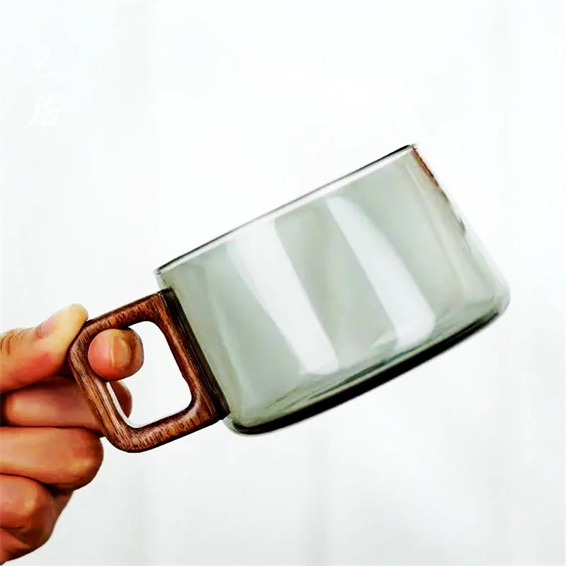 Clear glass mug with wooden handle held by a hand on a white background