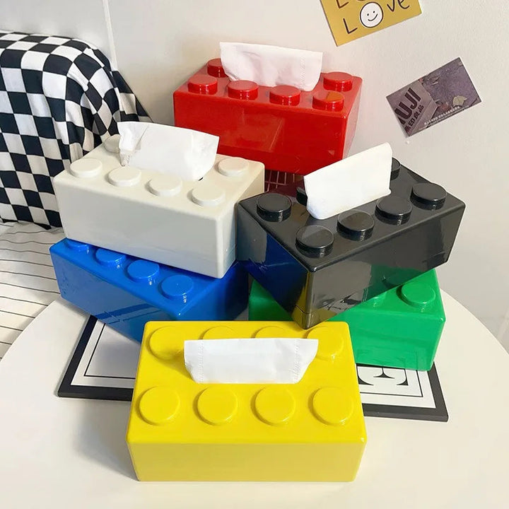 Colorful block-shaped tissue boxes on a table with a checkered bag in the background.