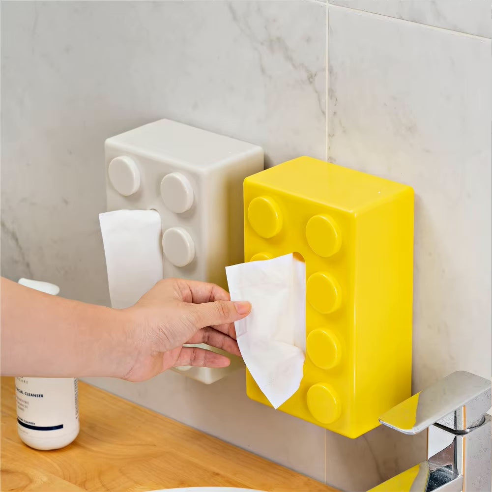 Yellow and white brick-shaped tissue holder on a tiled wall with a hand reaching for a tissue.