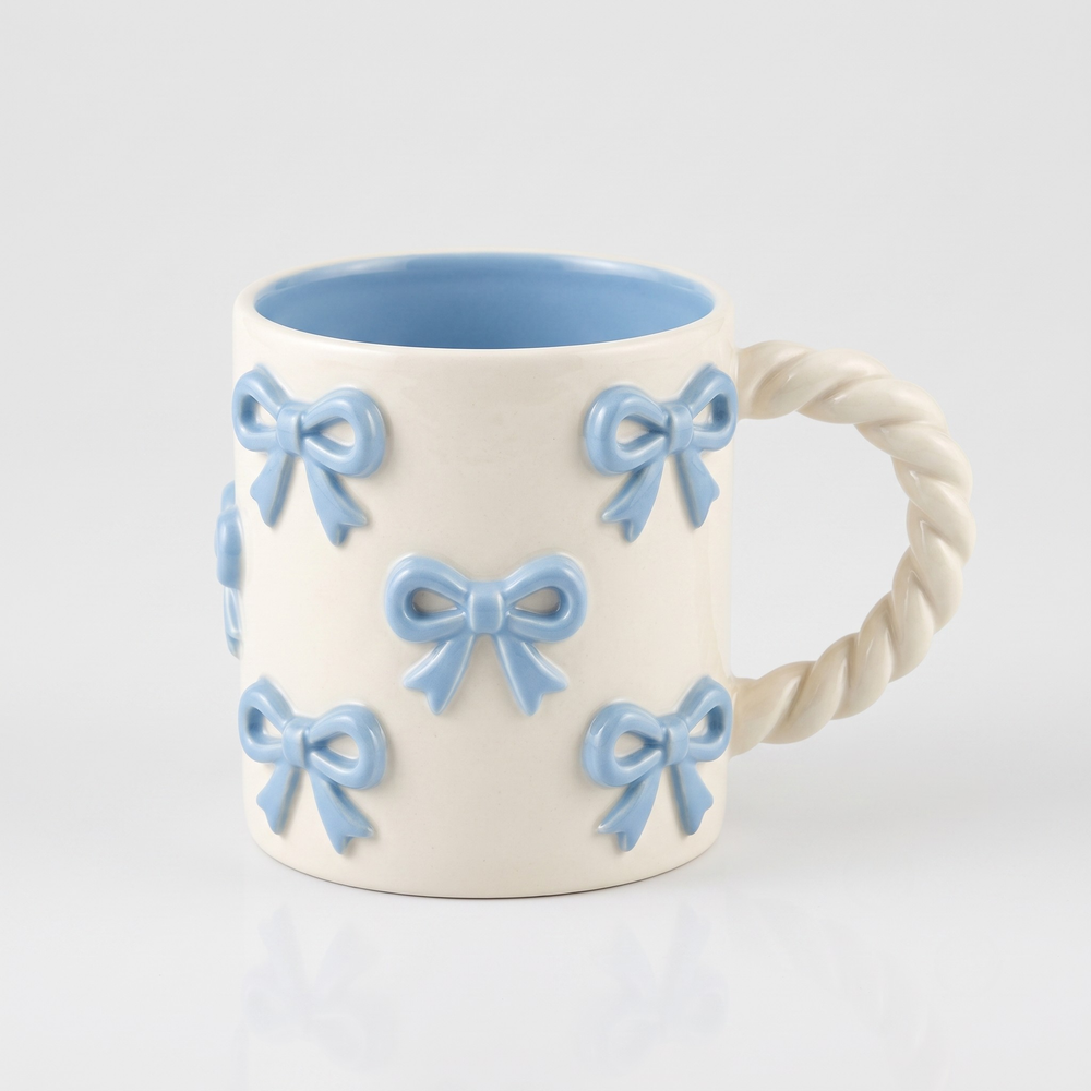 An off-white ceramic mug with a twisted rope handle, decorated with light blue 3D ribbon bows, featuring a light blue interior.