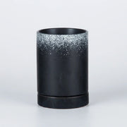 A black cylindrical candle holder or vase with a textured, glittery silver gradient near the rim, set against a clean white background.