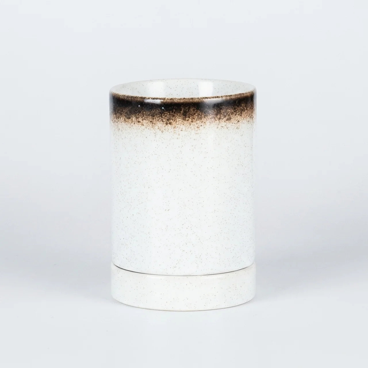 A cylindrical ceramic cup or tumbler with a white speckled glaze, featuring a dark brown gradient band near the rim, set against a plain light gray background.