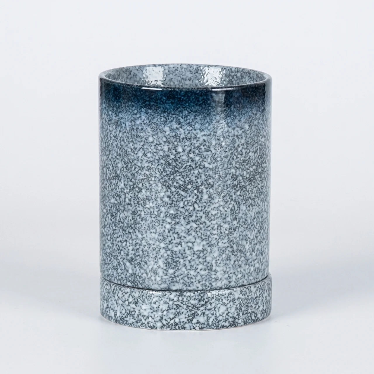 A cylindrical ceramic cup with a textured, speckled glaze that transitions from a dark blue at the rim to a light gray-blue at the base, set against a plain white background.