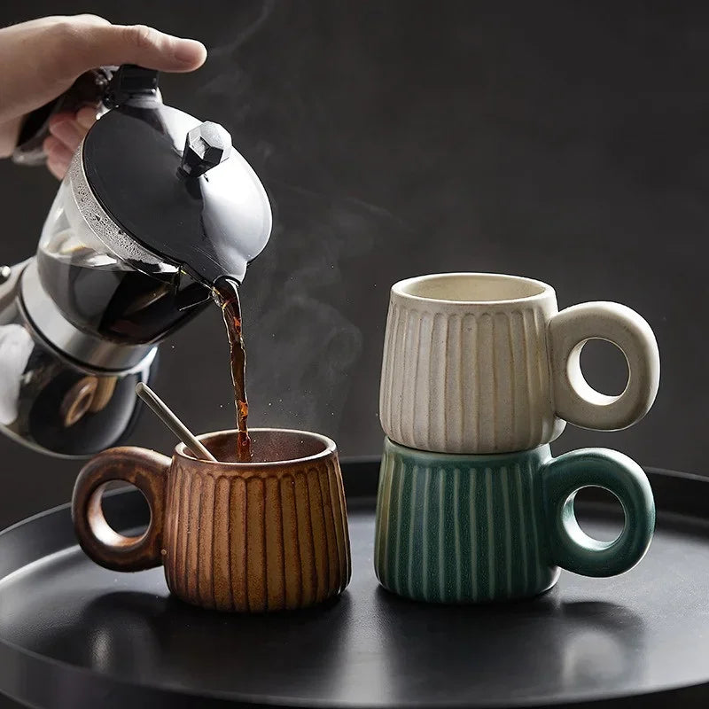 Person pouring coffee from a pot into two ceramic mugs on a dark surface.