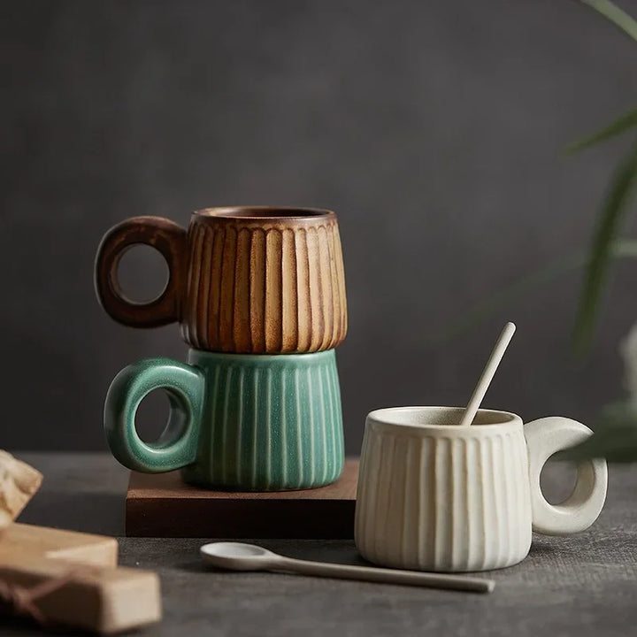 Three ceramic mugs in different colors with striped patterns on a dark surface.