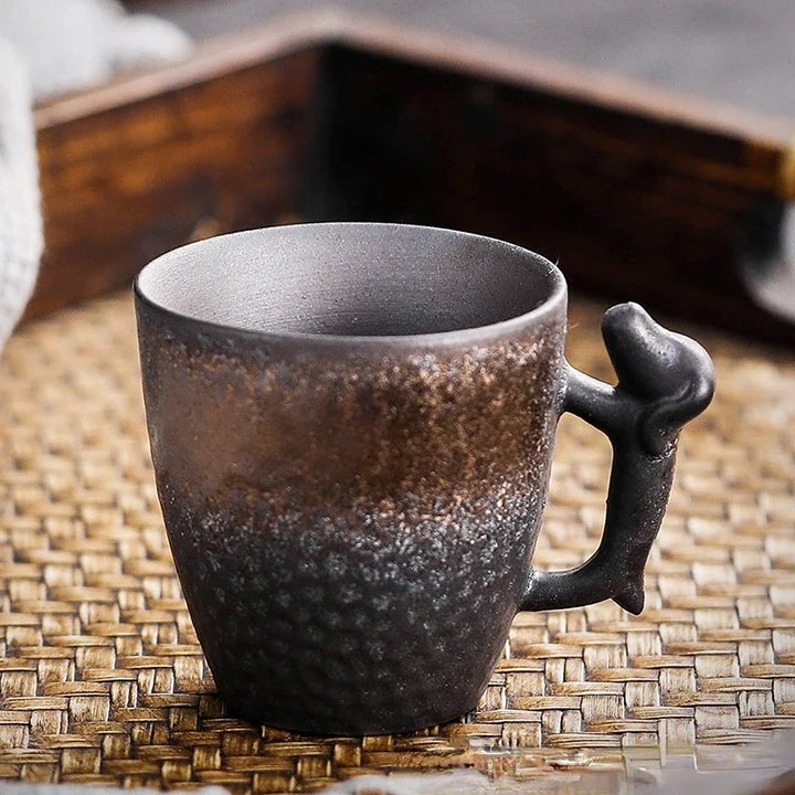 Dark brown ceramic mug with a unique handle on a woven mat