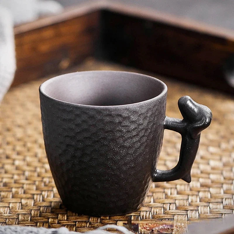 Dark ceramic mug with a unique handle on a woven mat