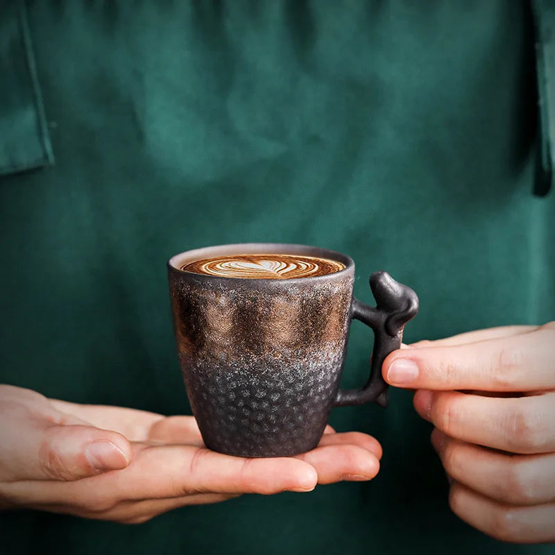 Person holding a textured coffee cup with a decorative handle against a green background