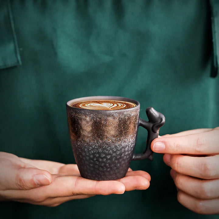 Person holding a textured coffee cup with a decorative handle against a green background