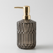 A faceted dark gray glass pump bottle with a shiny gold metallic dispenser, shown on a light gray background.