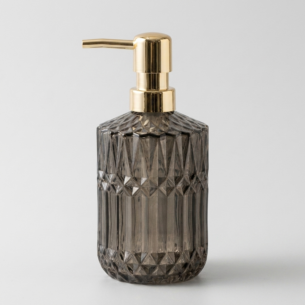 A faceted dark gray glass pump bottle with a shiny gold metallic dispenser, shown on a light gray background.
