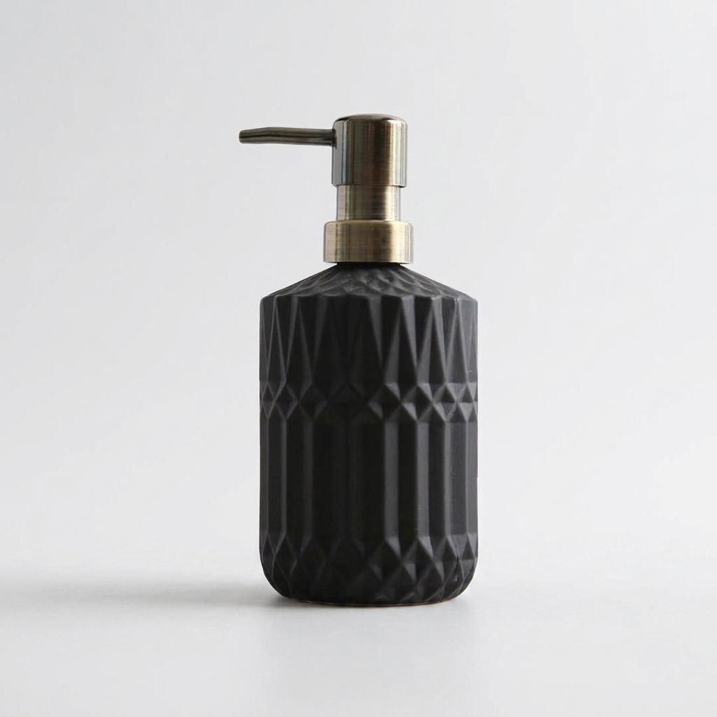 A black textured soap dispenser bottle with a geometric faceted pattern and a brushed brass pump, shown on a clean light gray background.