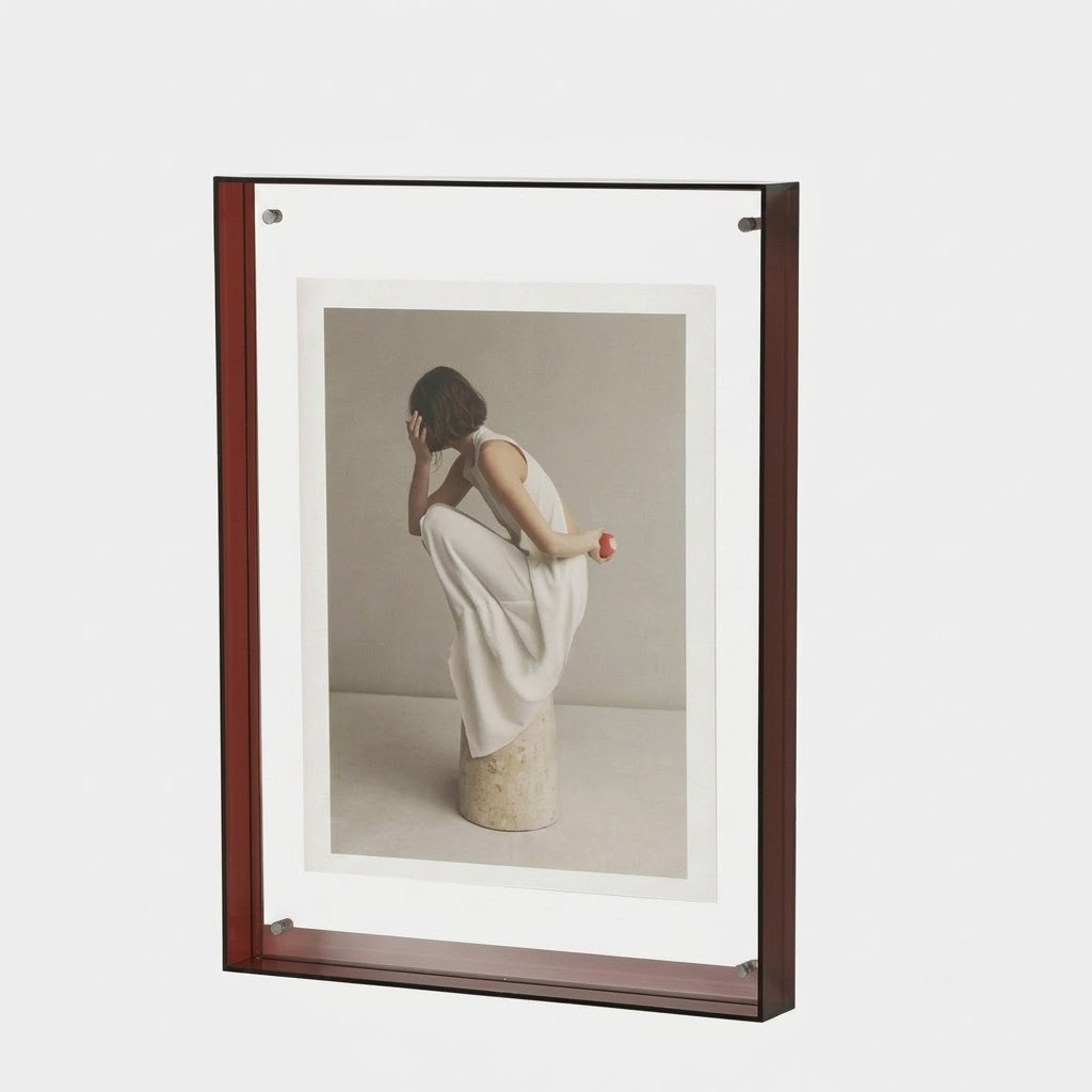 A framed art print featuring a photograph of a woman in a white dress sitting on a stone pedestal, set in a dark reddish-brown frame with a white mat border, shown against a light gray background.