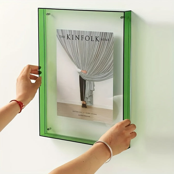 Person holding a green-framed magazine cover featuring 'The Kinfolk Home' on a white wall.