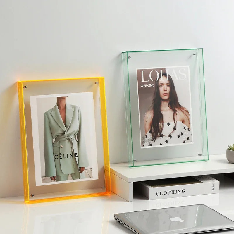 Two framed pictures on a shelf with a laptop and books below.