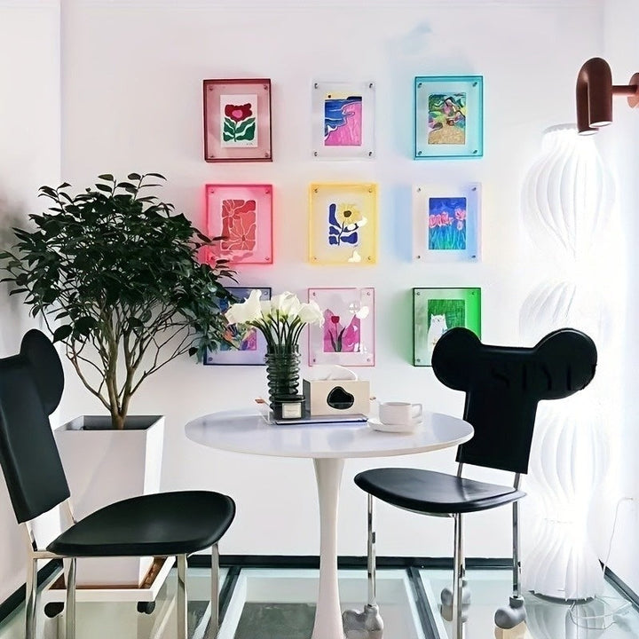 Modern interior with a round white table and black chairs, colorful wall art, and a plant.