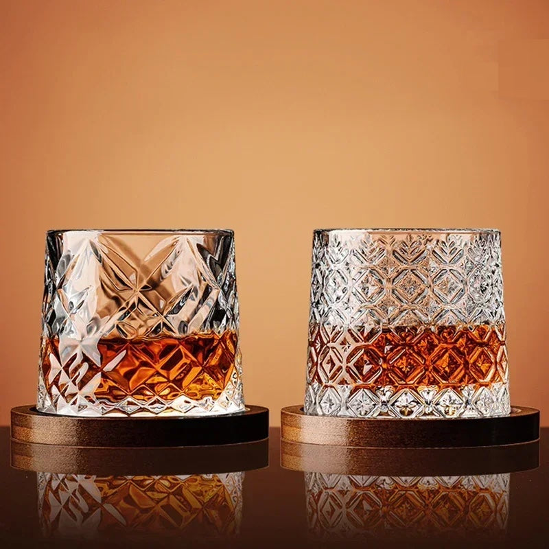 Two crystal glasses filled with a amber liquid on wooden coasters against an orange background