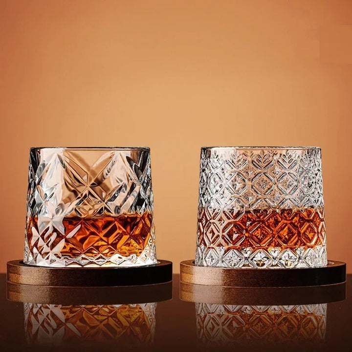 Two crystal glasses filled with a amber liquid on wooden coasters against an orange background
