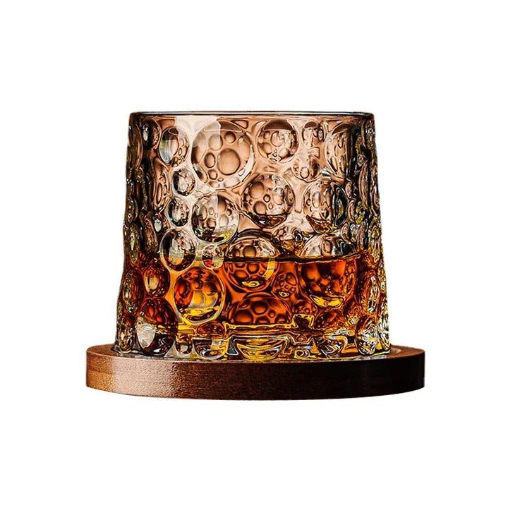 Glass with bubble design filled with a amber liquid on a wooden coaster.