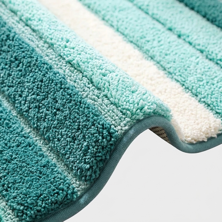 A close-up of a plush bath mat with alternating teal and off-white stripes, showing its thick textured pile and folded corner.