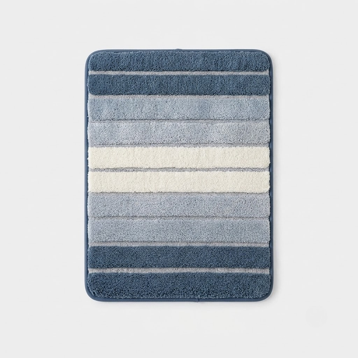 A rectangular bath mat with rounded corners, featuring horizontal stripes in shades of blue, gray, and cream, shown against a light gray background.