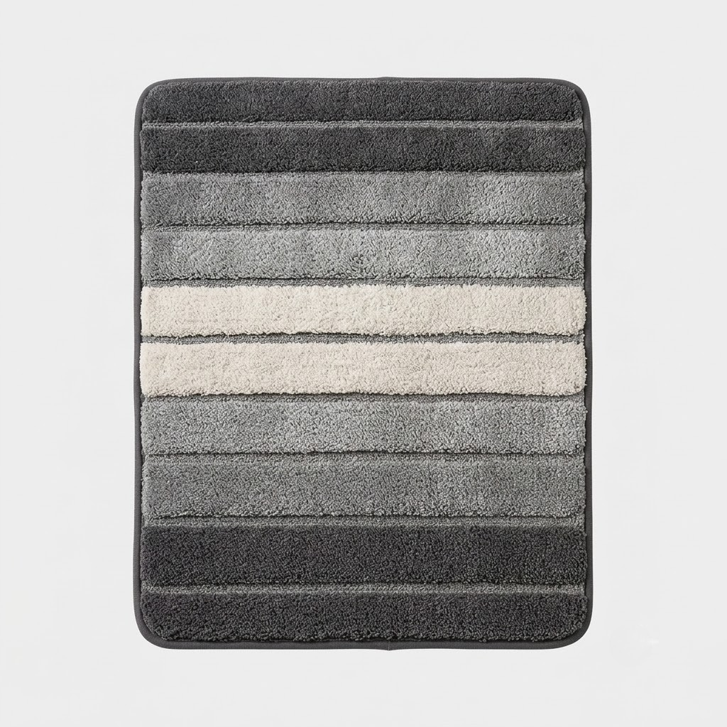 A rectangular bath mat with rounded corners, featuring horizontal striped texture in shades of dark gray, medium gray, and a central off-white stripe, shown against a light gray background.