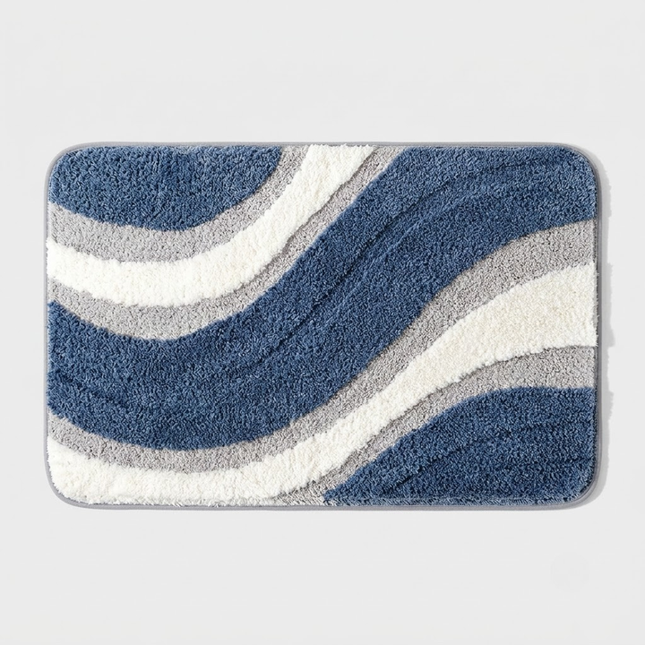 A rectangular bath mat with rounded corners featuring a wavy, flowing pattern in navy blue, medium blue, gray, and white, set against a light gray background.