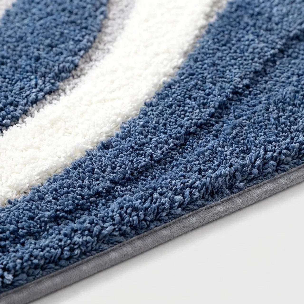 A close-up of a plush shag rug with diagonal stripes in blue and white, showing the thick textured pile and a gray binding edge.