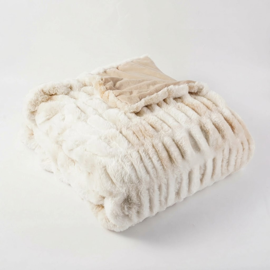 A folded plush faux fur blanket in cream and beige tones, showing a ribbed texture and a smooth beige lining, photographed on a seamless white background.