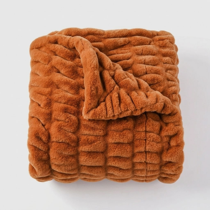 A folded chunky knit blanket in a warm rust or burnt orange color, shown on a clean light gray background.
