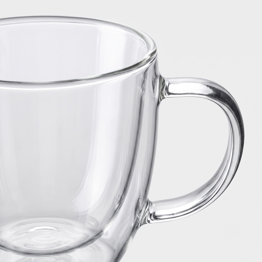 Clear glass mug with a thick curved handle, shown close-up against a light gray background.