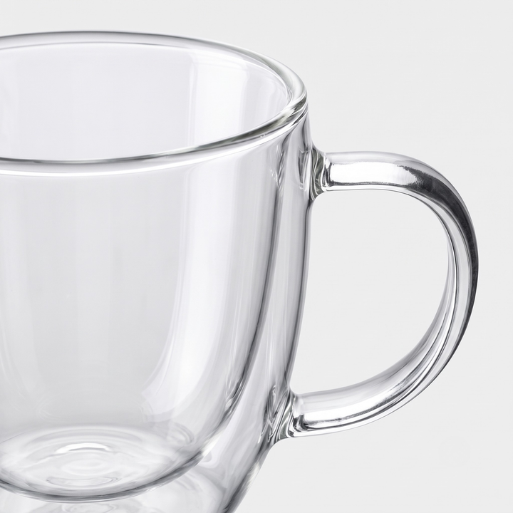 Clear glass mug with a thick curved handle, shown close-up against a light gray background.