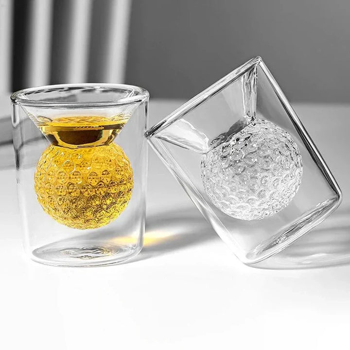 Two glass shot glasses with textured balls inside on a light surface.