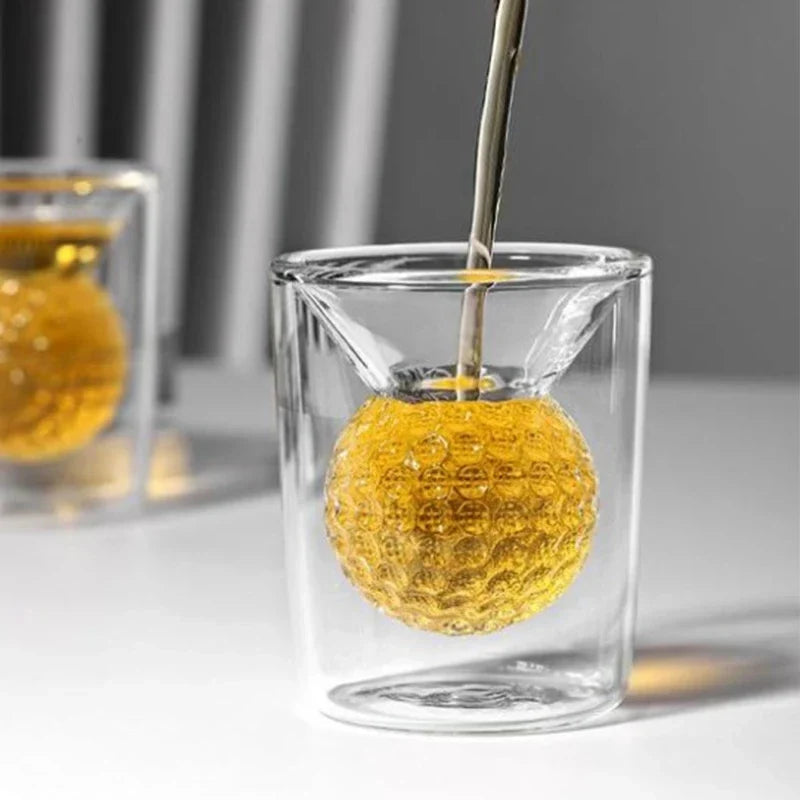 Glass with a textured yellow ball being filled with a liquid using a spoon.