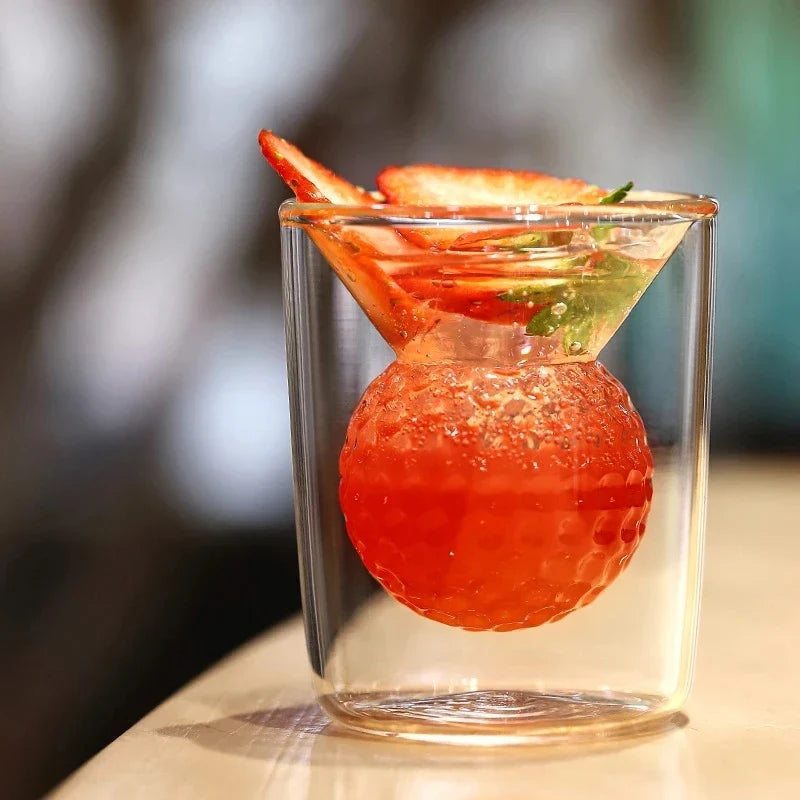 Cocktail with a red fruit sphere and garnish in a clear glass on a blurred background