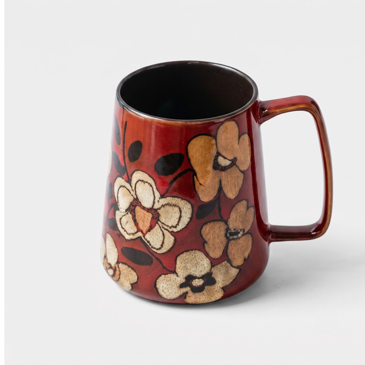 A ceramic mug with a dark reddish-brown base, decorated with a pattern of beige and light brown flowers with dark brown centers and stems. The mug features a thick, rounded handle and is photographed on a clean, light gray background.