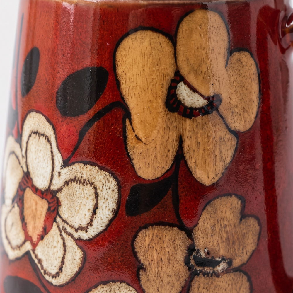 Close-up of a glossy red ceramic mug decorated with hand-painted floral motifs in beige, brown, and black.