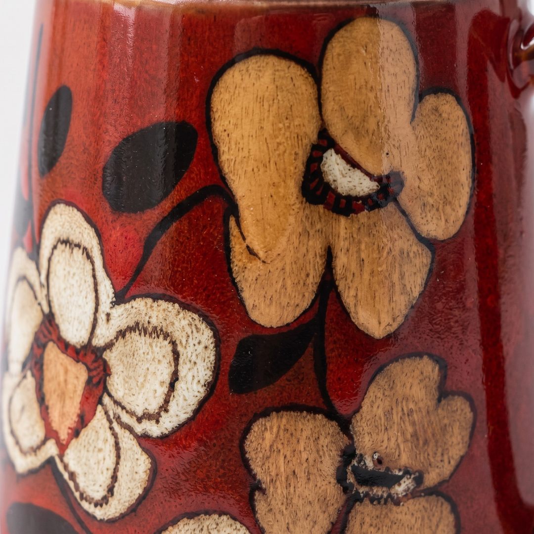 Close-up of a glossy red ceramic mug decorated with hand-painted floral motifs in beige, brown, and black.