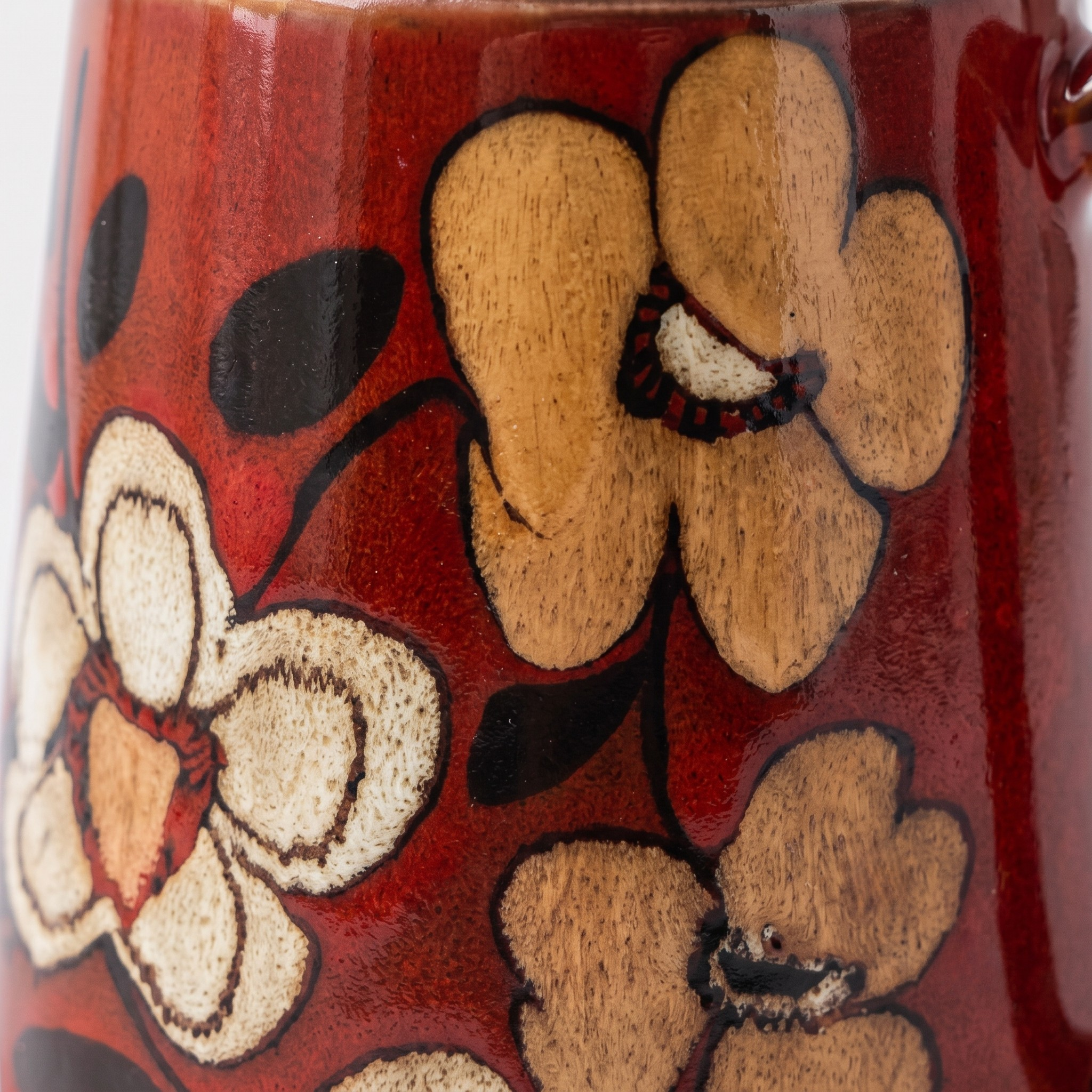Close-up of a glossy red ceramic mug decorated with hand-painted floral motifs in beige, brown, and black.