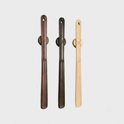 Three long wooden cleaning tools with circular handles, shown vertically on a light gray background. The left tool is dark brown, the middle is very dark gray/black, and the right is light natural wood.