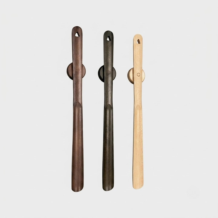 Three long wooden cleaning tools with circular handles, shown vertically on a light gray background. The left tool is dark brown, the middle is very dark gray/black, and the right is light natural wood.