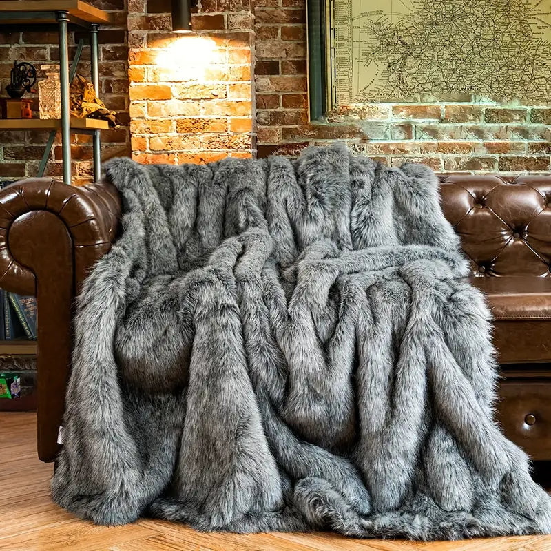 Gray fur throw blanket draped over a brown leather sofa against a brick wall.