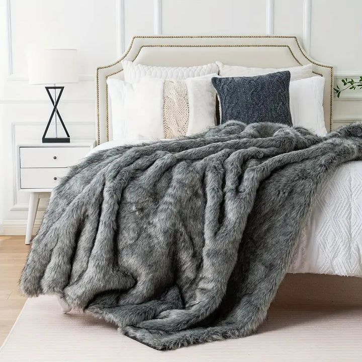 Gray fur throw blanket draped over a bed with white bedding and pillows.