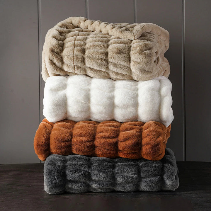 Stack of four textured blankets in beige, white, brown, and gray on a dark surface with a gray background.