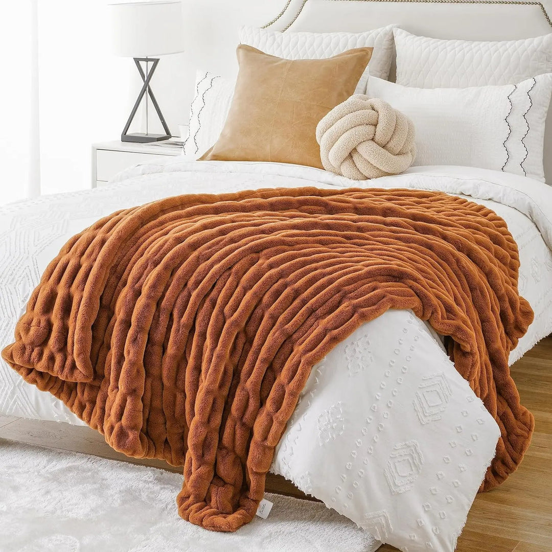 Brown blanket draped over a white bed with decorative pillows.